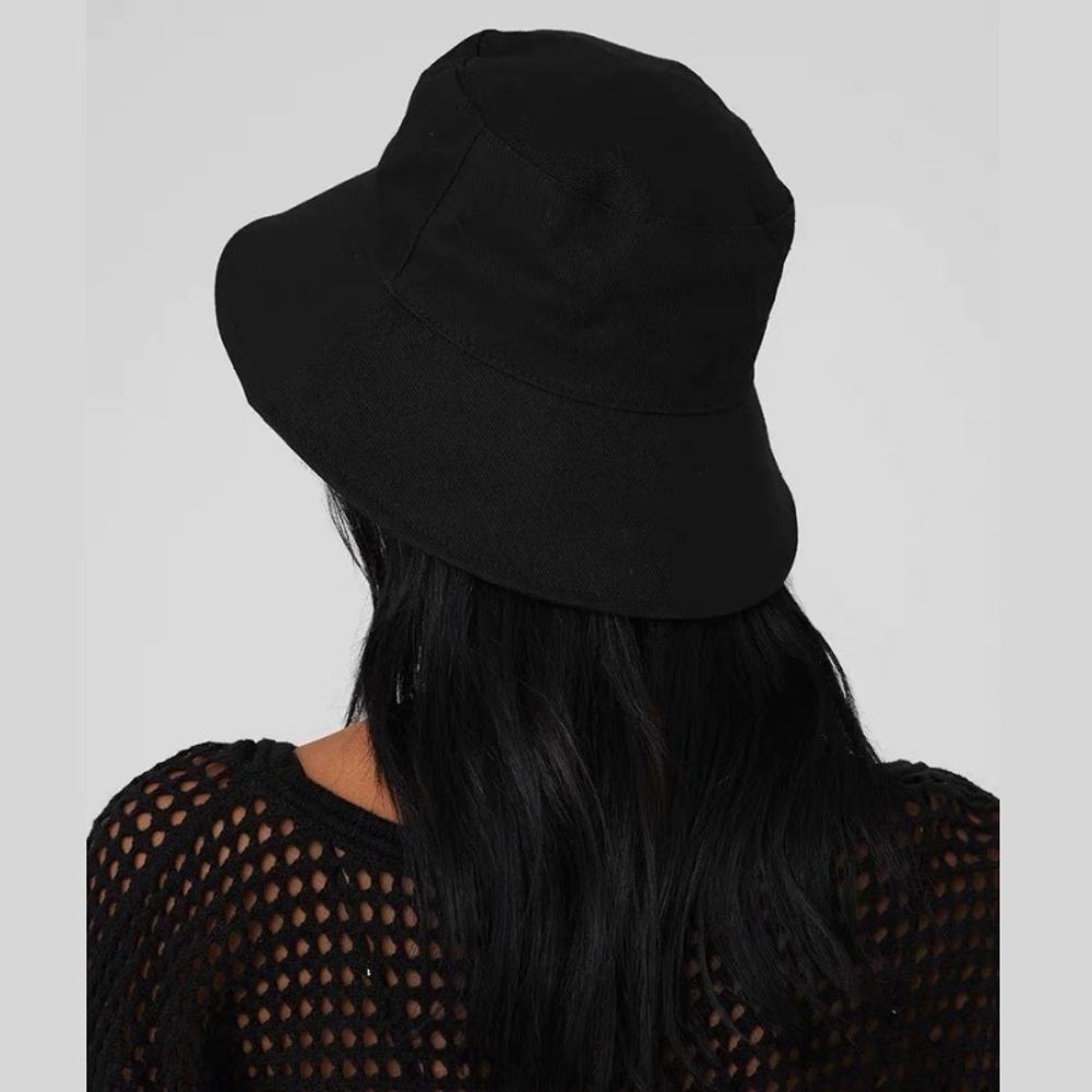 Black cotton wide brim bucket hat worn by woman with long black hair and mesh black top