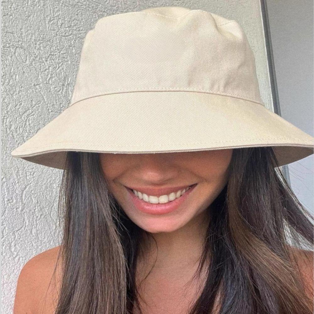 Woman wearing a beige cotton wide brim bucket hat smiling in natural light