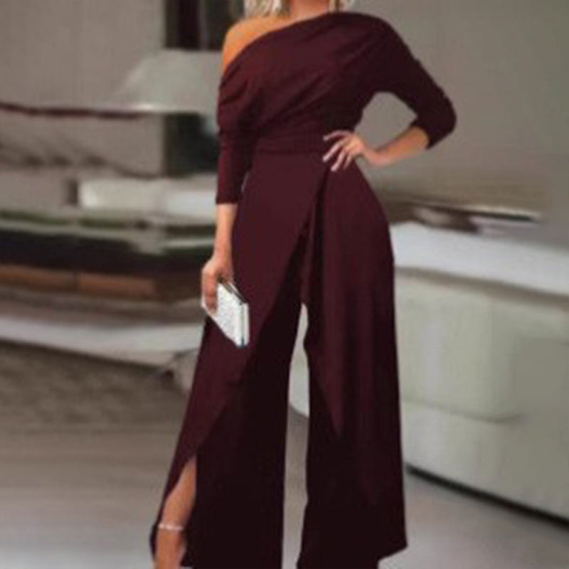 Woman wearing a maroon formal party jumpsuit with pants slit and asymmetrical one-shoulder design