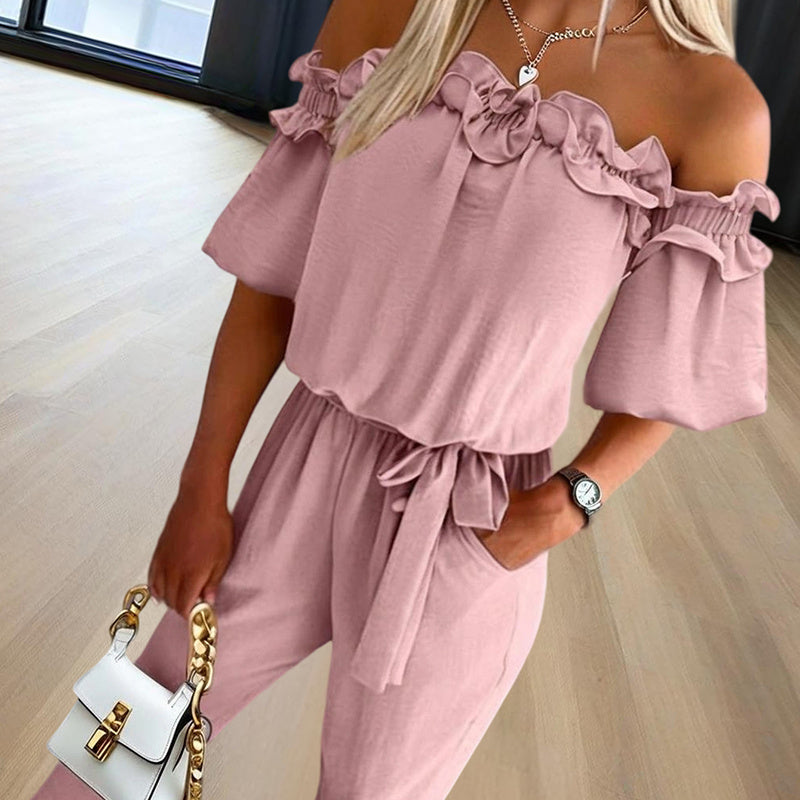 Woman wearing an elegant off-shoulder jumpsuit for women in soft pink with ruffle details and a waist tie
