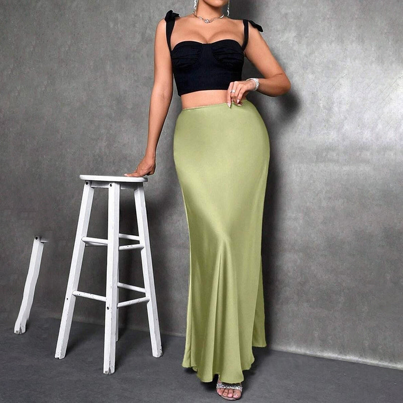 Woman wearing an elegant satin midi skirt in light green paired with a black cropped top