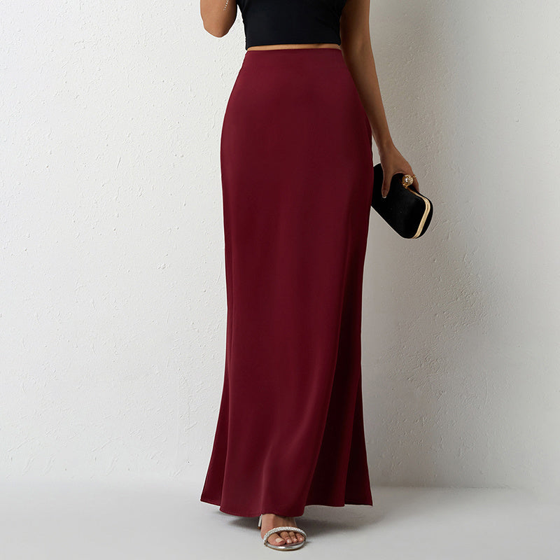 Woman wearing elegant satin midi skirt in deep burgundy paired with black crop top and clutch