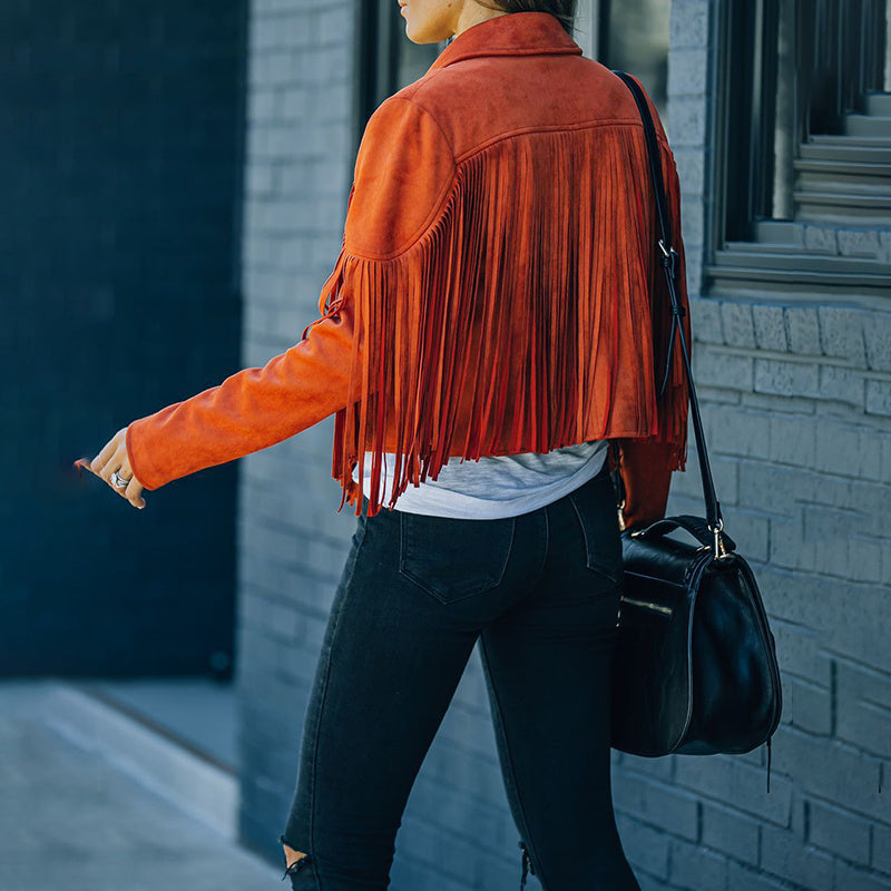 Back view of a woman wearing an orange women's faux suede fringe jacket with black jeans and black handbag