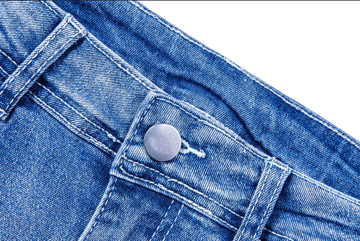 Close-up of blue womens ripped jean shorts denim fabric with metal button and stitching detail