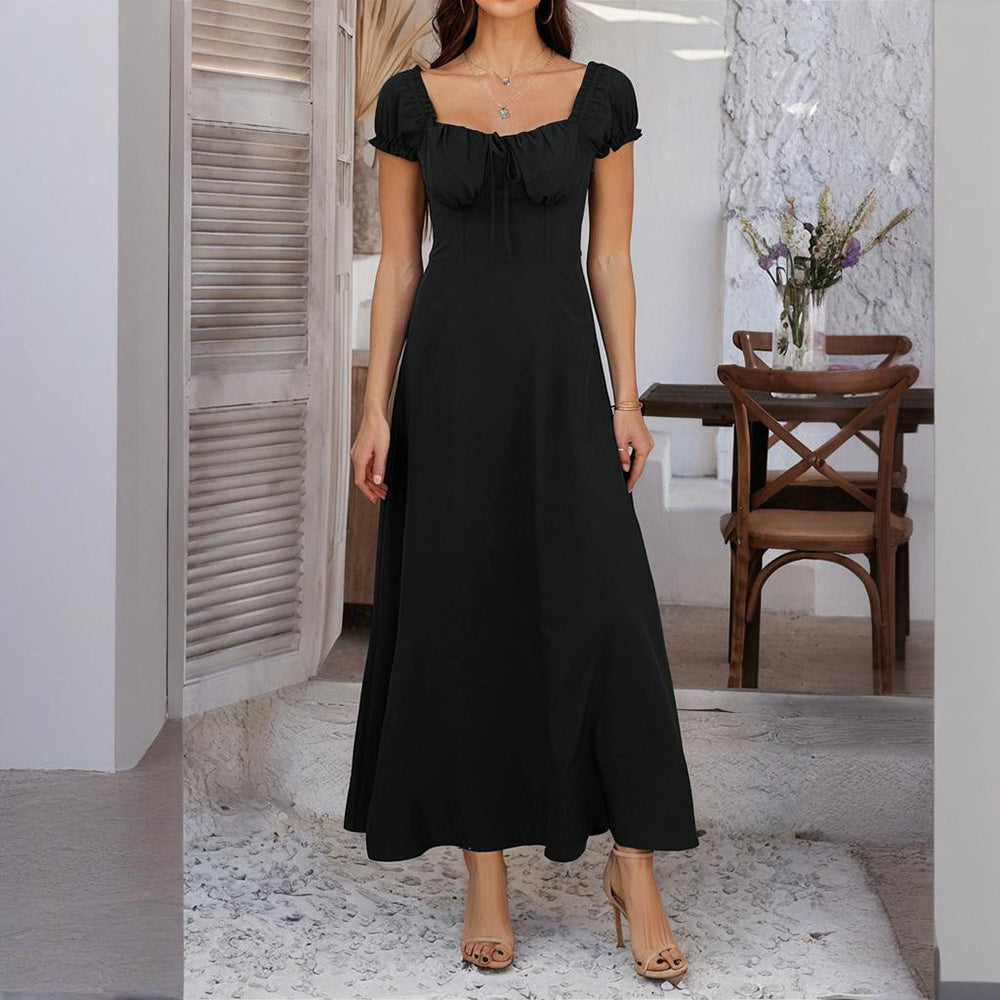 Woman wearing a black bohemian backless maxi dress standing indoors near wooden chair and table