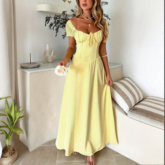 Woman wearing a yellow bohemian backless maxi dress standing indoors holding a white flower