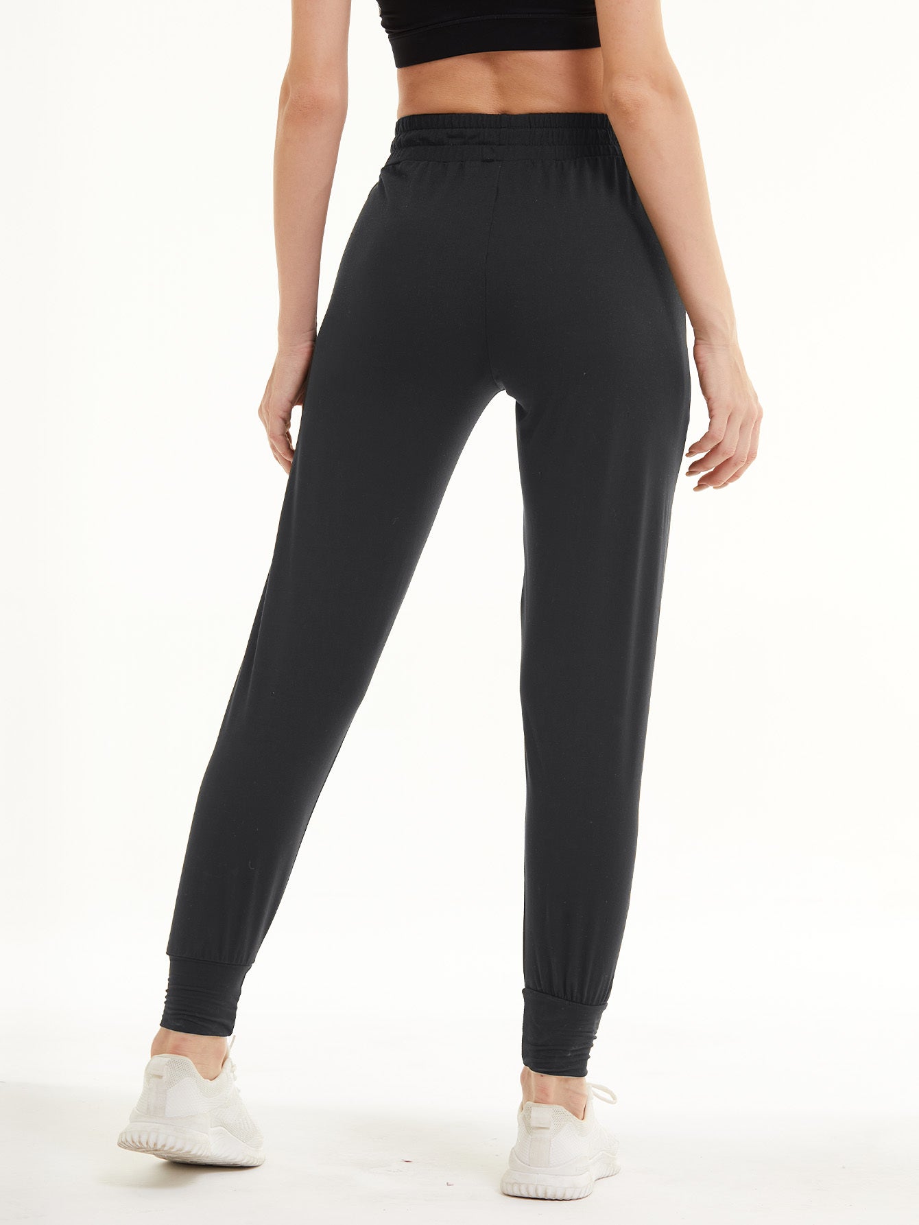 Back view of woman wearing dark gray cropped sweatpants with elastic waistband and ankle cuffs