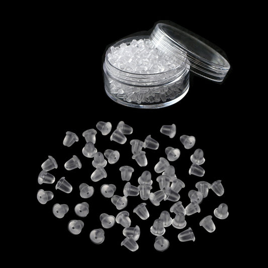 Clear silicone earring backs in a transparent container and scattered on black background