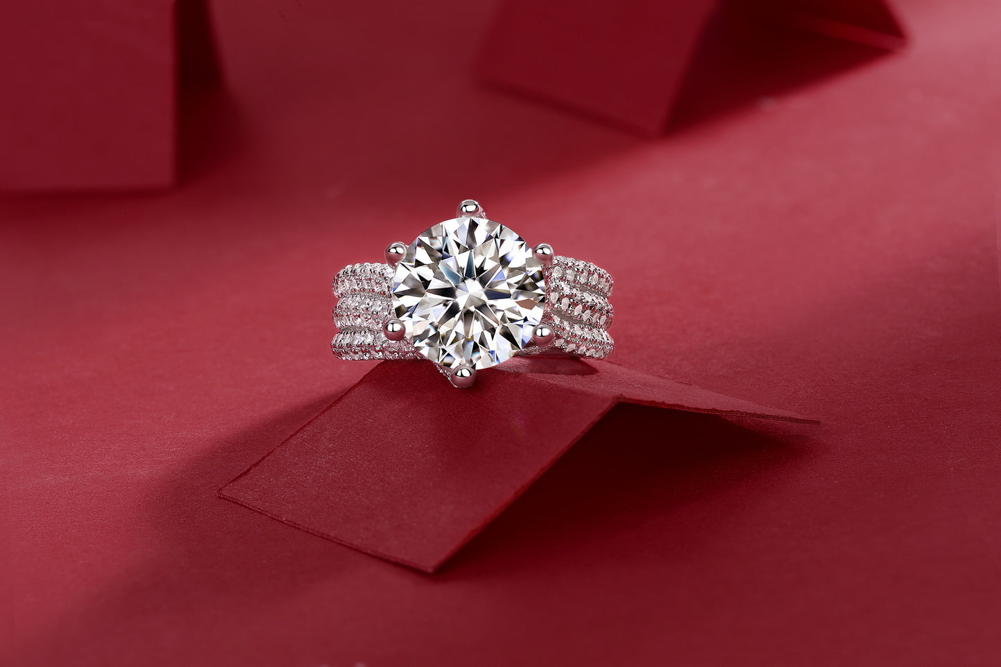 Luxury moissanite diamond ring with a large round center stone and triple band setting on red background
