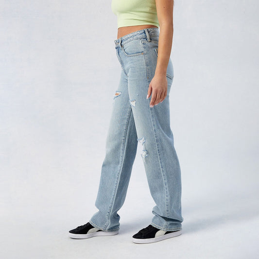 Light blue distressed women's high-waist wide leg jeans styled with black sneakers and a cropped top
