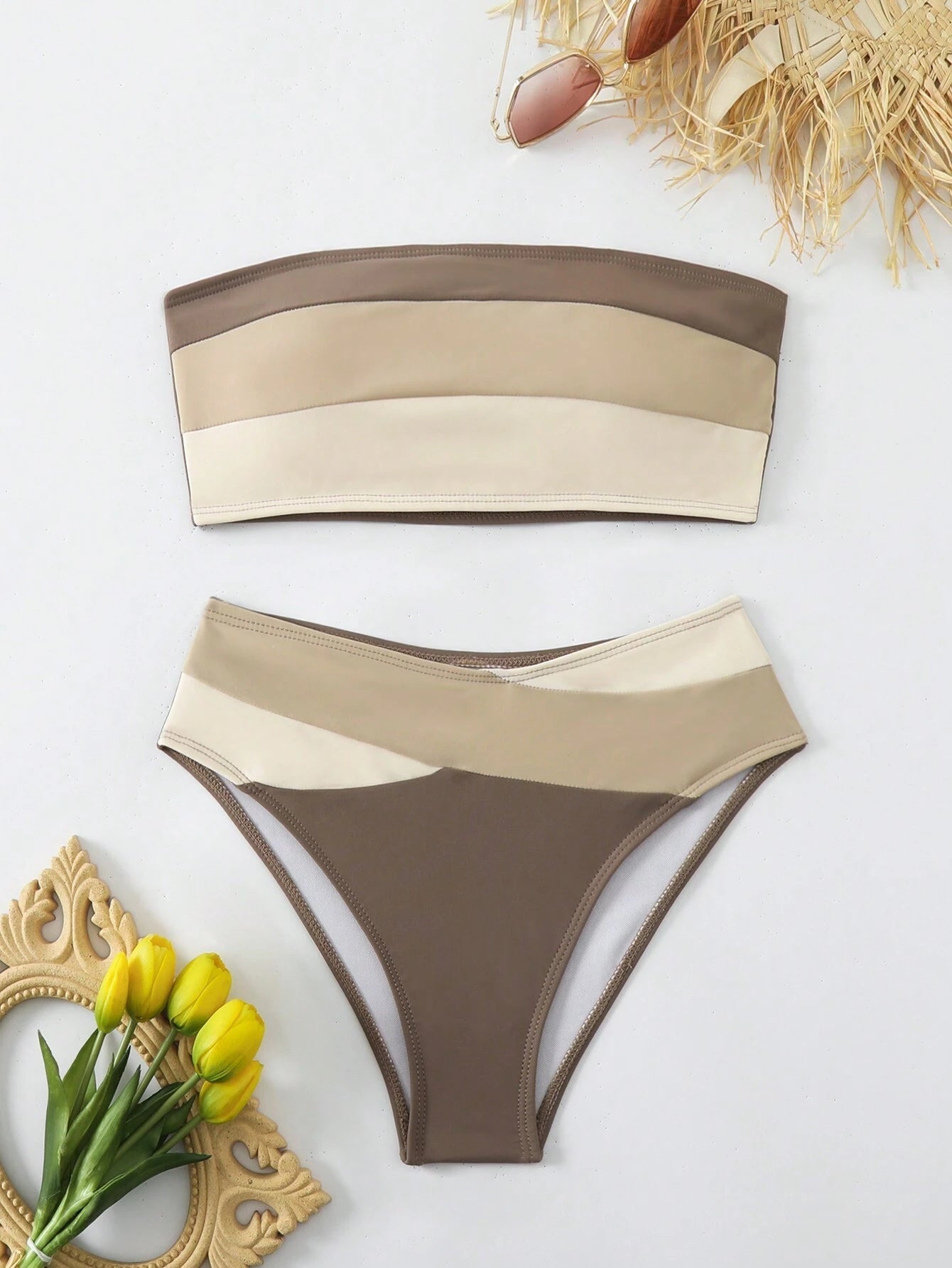 Stylish women's two-piece swimsuit with neutral beige and brown color blocks laid flat with sunglasses and hat